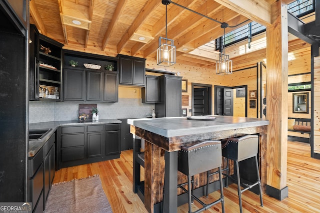 kitchen with a center island, wood walls, light wood-type flooring, decorative light fixtures, and a kitchen bar