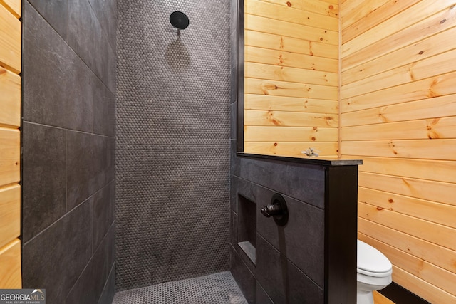 bathroom with a tile shower, toilet, and wooden walls