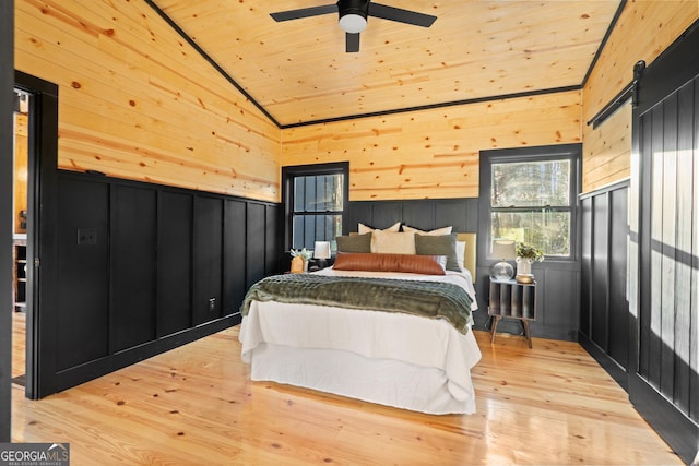 bedroom featuring wood walls, light hardwood / wood-style flooring, ceiling fan, a barn door, and wood ceiling