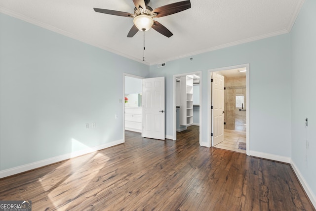 unfurnished bedroom featuring ceiling fan, dark wood-type flooring, crown molding, a walk in closet, and a closet