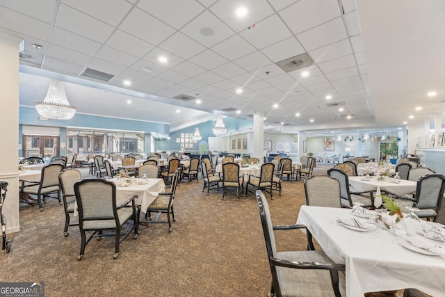 dining area with carpet flooring, a drop ceiling, and a notable chandelier