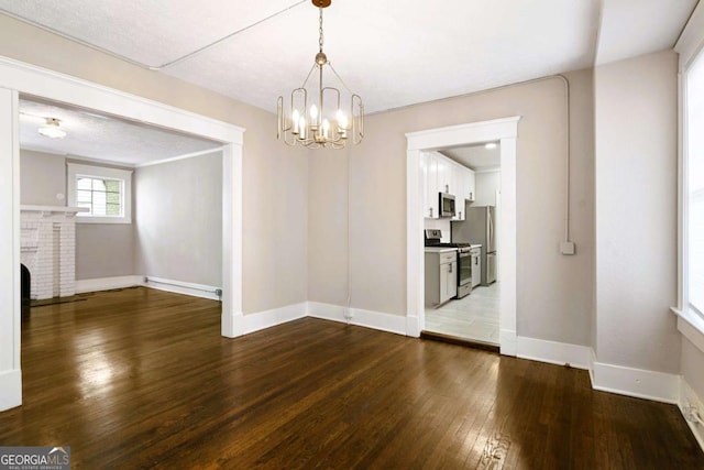 unfurnished dining area featuring hardwood / wood-style floors, a brick fireplace, and an inviting chandelier