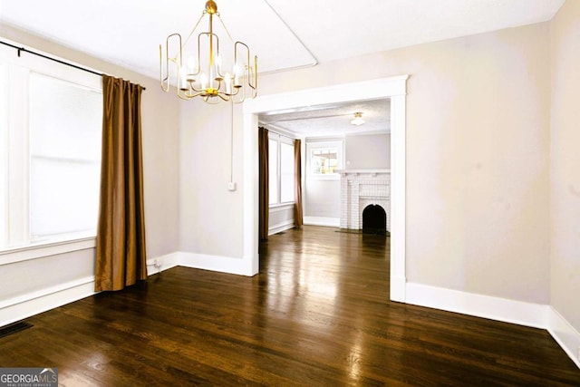 unfurnished dining area with an inviting chandelier, a brick fireplace, and dark wood-type flooring