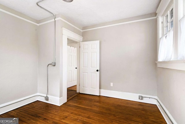 spare room featuring dark wood-type flooring, a textured ceiling, and ornamental molding