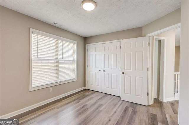 unfurnished bedroom with a closet, a textured ceiling, and light wood-type flooring