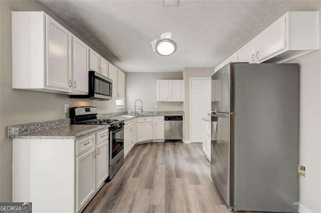 kitchen with light stone countertops, light wood-type flooring, a textured ceiling, stainless steel appliances, and white cabinets