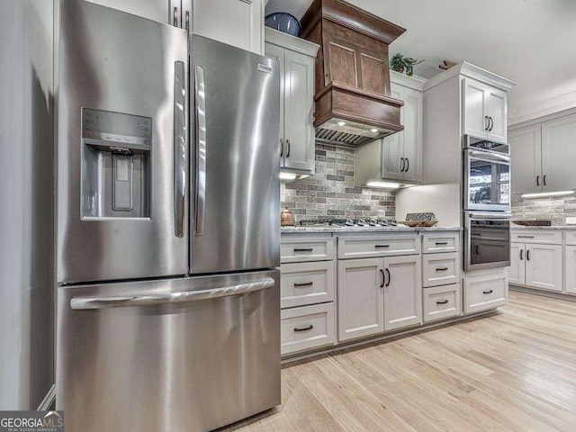 kitchen featuring tasteful backsplash, custom range hood, stainless steel appliances, and light hardwood / wood-style flooring