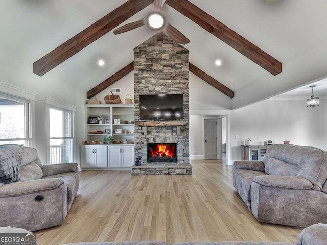 living room featuring beam ceiling, ceiling fan, a stone fireplace, light hardwood / wood-style flooring, and high vaulted ceiling