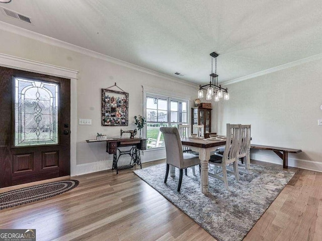 dining space with a textured ceiling, wood-type flooring, and ornamental molding