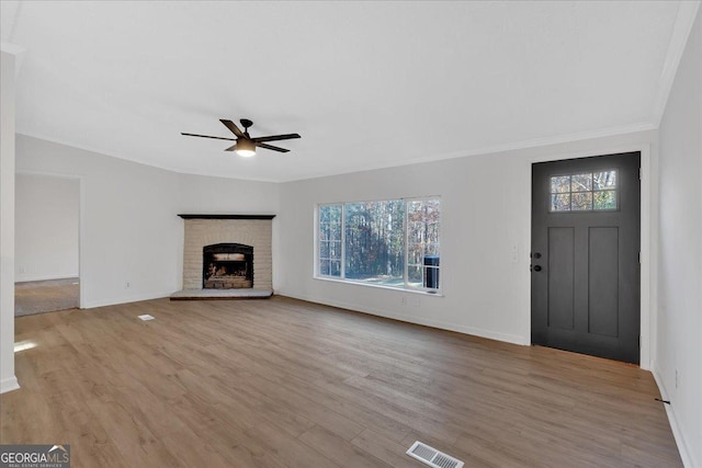 unfurnished living room featuring a brick fireplace, crown molding, ceiling fan, and light wood-type flooring