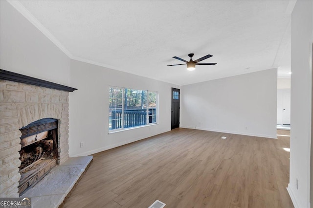 unfurnished living room featuring ceiling fan, crown molding, light hardwood / wood-style floors, a textured ceiling, and a fireplace