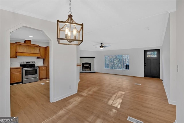 kitchen with ceiling fan with notable chandelier, light hardwood / wood-style flooring, electric range, a fireplace, and decorative light fixtures