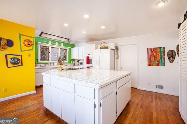 kitchen with white fridge with ice dispenser, tile countertops, wood-type flooring, a center island with sink, and white cabinets