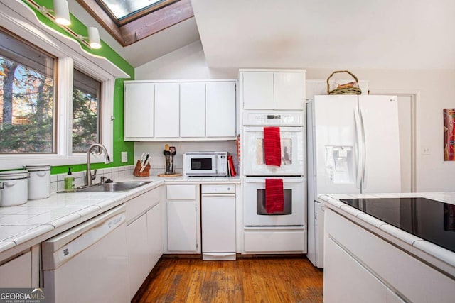 kitchen with tile countertops, white appliances, lofted ceiling with skylight, white cabinets, and sink