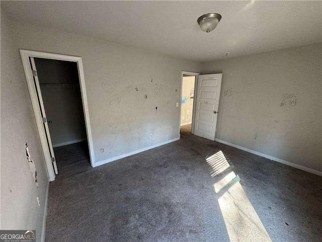 unfurnished bedroom featuring a walk in closet, a closet, and dark colored carpet