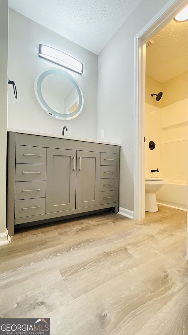 bathroom with washtub / shower combination, toilet, wood-type flooring, and a textured ceiling