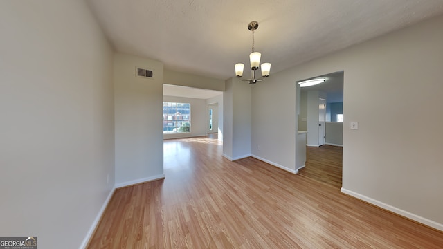 unfurnished dining area with light hardwood / wood-style floors, a textured ceiling, and an inviting chandelier