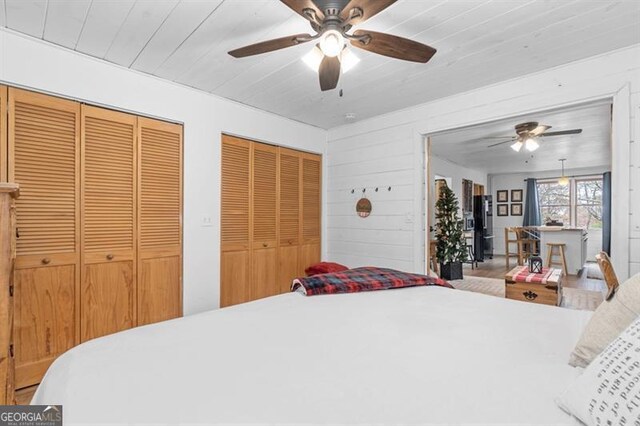 bedroom featuring multiple closets, ceiling fan, wooden ceiling, and wood walls