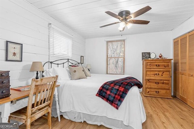 bedroom with ceiling fan, a closet, wooden walls, and light hardwood / wood-style flooring