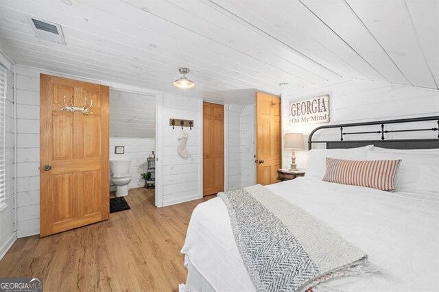 bedroom with ensuite bath, wood walls, light hardwood / wood-style floors, and lofted ceiling