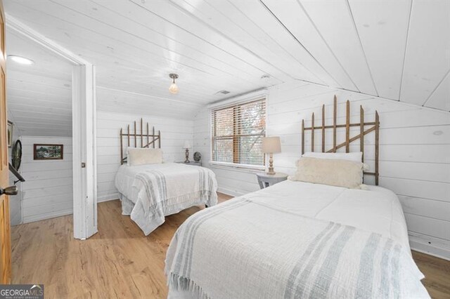 bedroom featuring wooden walls, vaulted ceiling, and light wood-type flooring