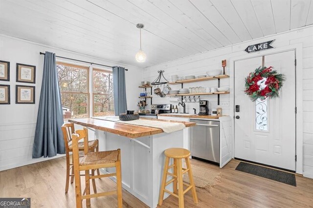 kitchen with a kitchen bar, appliances with stainless steel finishes, light hardwood / wood-style floors, pendant lighting, and butcher block countertops