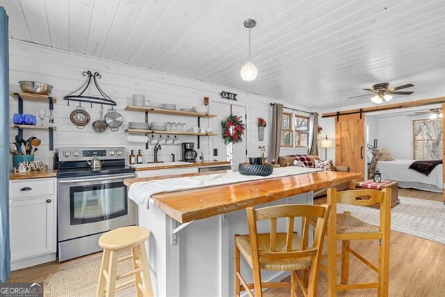 kitchen featuring ceiling fan, stainless steel range with electric cooktop, a barn door, a breakfast bar area, and butcher block counters