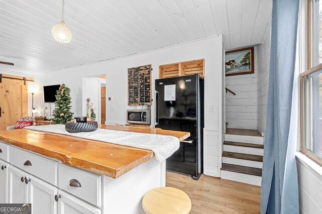 kitchen featuring black fridge, pendant lighting, a barn door, light hardwood / wood-style flooring, and white cabinetry