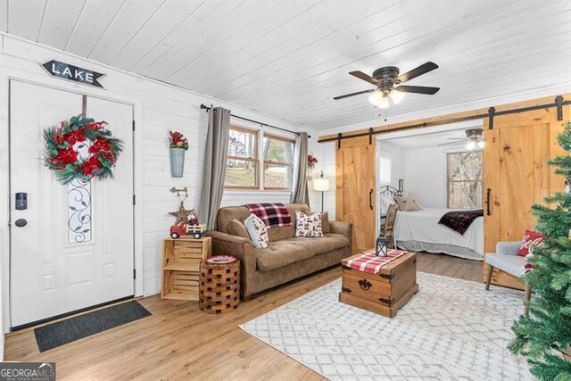 living room featuring wooden ceiling, wooden walls, hardwood / wood-style flooring, ceiling fan, and a barn door