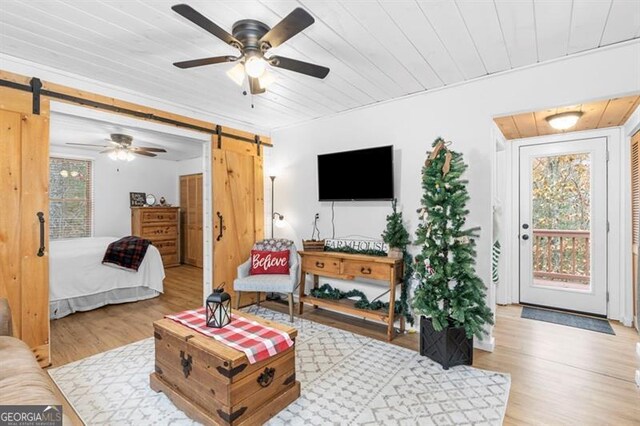 living room with light wood-type flooring, a barn door, and ceiling fan