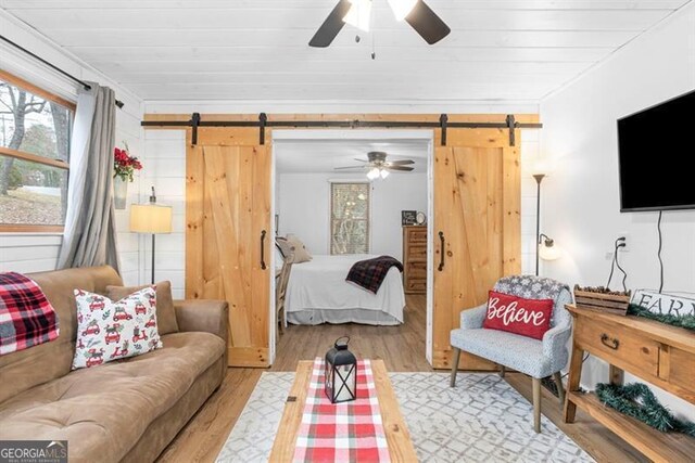 bedroom with ceiling fan, a barn door, light hardwood / wood-style floors, and crown molding