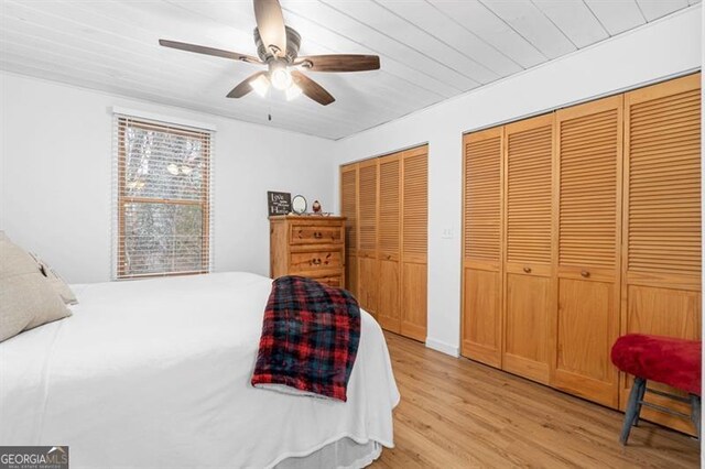 bedroom with ceiling fan, light hardwood / wood-style floors, and multiple closets