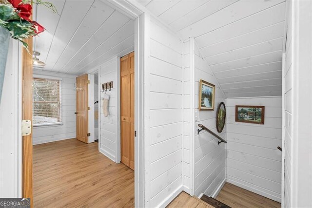 hallway with lofted ceiling, light wood-type flooring, and wooden walls