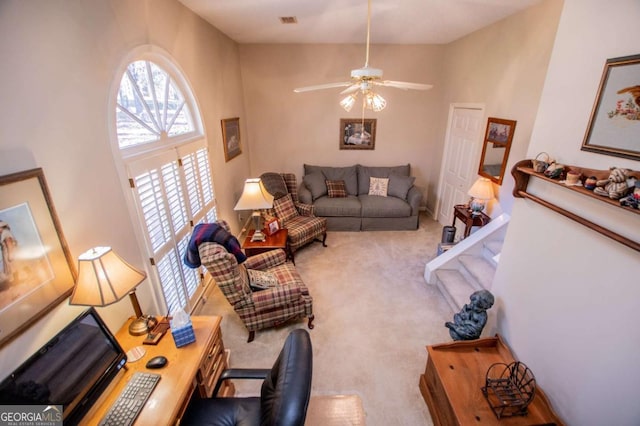 carpeted living room featuring ceiling fan and a towering ceiling