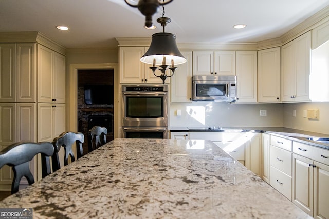 kitchen with ornamental molding, stainless steel appliances, pendant lighting, cream cabinets, and a breakfast bar area