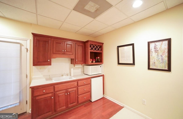 kitchen featuring sink, a drop ceiling, white appliances, and light hardwood / wood-style flooring