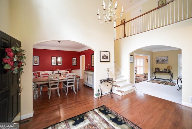 interior space featuring wood-type flooring, crown molding, a high ceiling, and an inviting chandelier