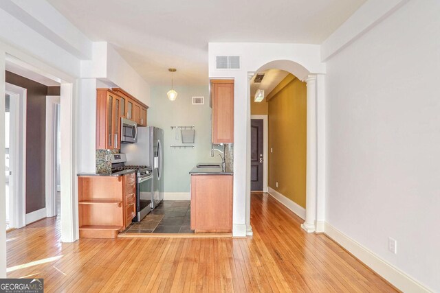 kitchen featuring sink, appliances with stainless steel finishes, backsplash, decorative columns, and dark hardwood / wood-style flooring