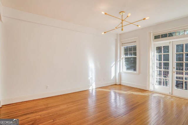 empty room featuring an inviting chandelier, light hardwood / wood-style floors, and french doors