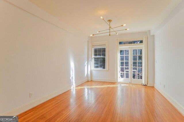 spare room with a notable chandelier, light hardwood / wood-style flooring, and french doors