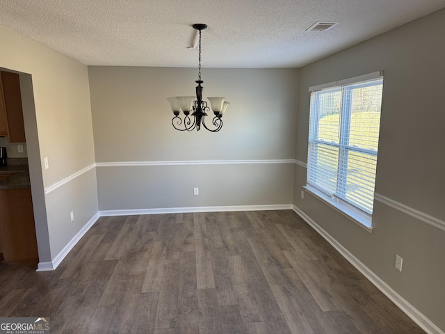 unfurnished dining area featuring dark hardwood / wood-style flooring, a textured ceiling, and an inviting chandelier