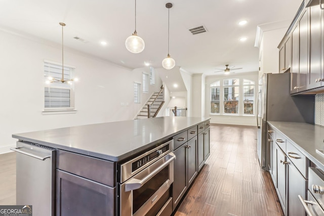 kitchen featuring pendant lighting, dark wood-type flooring, wall chimney range hood, a kitchen island, and stainless steel appliances