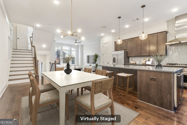 kitchen featuring dark brown cabinetry, wall chimney exhaust hood, dark hardwood / wood-style flooring, crown molding, and decorative light fixtures