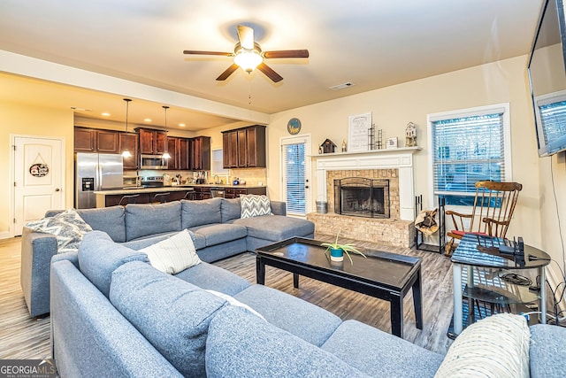 living room featuring ceiling fan, a fireplace, and light hardwood / wood-style floors