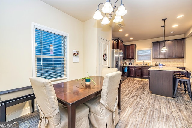 dining area with light hardwood / wood-style floors, an inviting chandelier, and sink