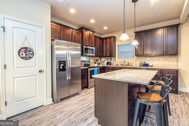 kitchen with tasteful backsplash, light stone counters, stainless steel appliances, pendant lighting, and a center island