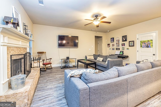 living room with ceiling fan, hardwood / wood-style flooring, and a brick fireplace