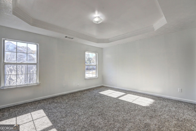 unfurnished room with dark colored carpet, ornamental molding, a raised ceiling, and a healthy amount of sunlight