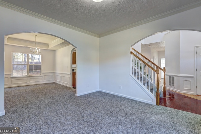 empty room featuring dark colored carpet, a notable chandelier, a textured ceiling, a tray ceiling, and ornamental molding