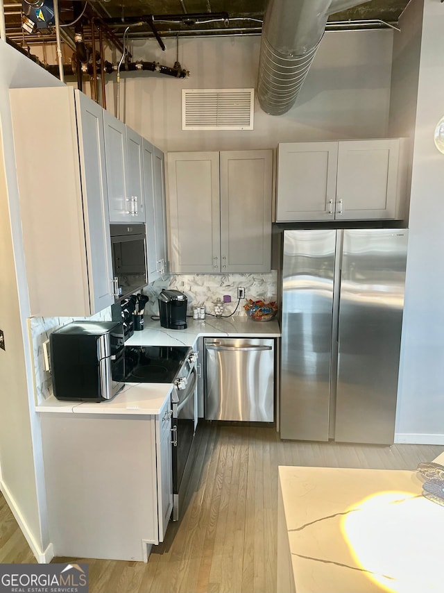 kitchen with light wood-type flooring, appliances with stainless steel finishes, and tasteful backsplash